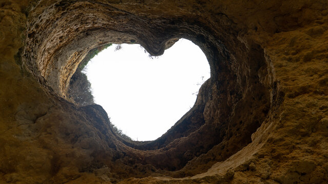 View of a heart-shaped opening in the ceiling of a limestone sea cave looking up towards the bright sky in Albufeira, Faro District, Portugal.