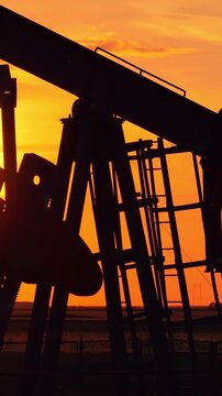 Silhouette of oil pump jack against a colorful beautiful sky with glowing clouds at sunset