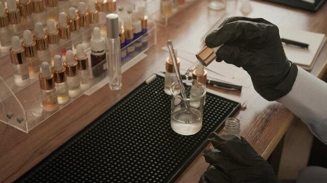 Perfumer wearing black gloves dripping liquid into beaker and stirring mixture with glass rod. Footage is perfect for cosmetics marketing, scent creation workshops, and beauty brand advertising