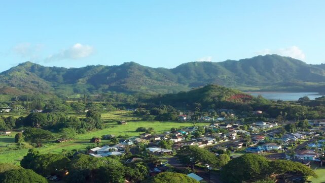 Aerial drone view of a beautiful neighborhood in Poipu, Koloa, with single-family houses surrounded by lush green nature and a majestic mountain range in the distance, Kauai, Hawaii. Cinematic flyover