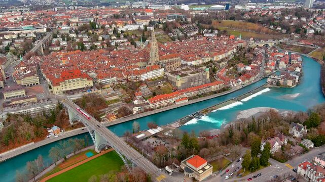4K aerial drone footage over Bern, Switzerland - UNESCO old town on Aare River meander, Bern M&uuml;nster Gothic spire, Kornhausbr&uuml;cke bridge with tram, turquoise river, and winter cityscape.