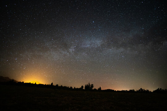 View of the Milky Way galaxy stretching across the starry night sky over a dark landscape with a bright orange glow on the horizon Jasenice, Zadar County, Croatia.