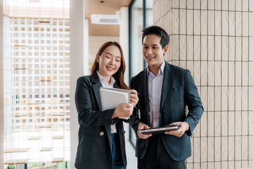 Young Asian business colleagues collaborating, smiling, and reviewing information on a digital tablet in a modern office environment