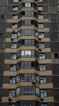 Symmetrical high-rise residential facade with repeating bay balconies, dark brick and beige panels, reflective windows, and air conditioner units creating geometric pattern