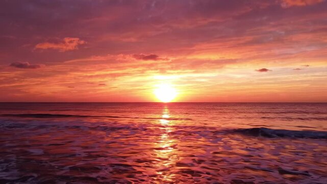 A breathtaking sunset paints the sky in vibrant hues of orange, pink, and purple, casting a warm glow over the tranquil ocean waves, creating a serene and picturesque scene.