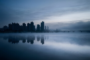 Fototapeta premium Han River Misty Dawn – Seoul Skyline Silhouette Reflected in Foggy Water