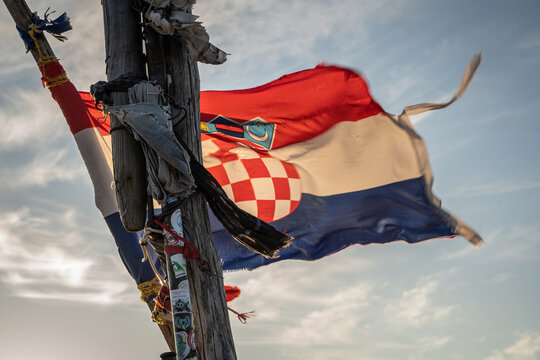 View of the Croatian flag waving in the wind from a wooden pole against a clear blue sky in Jasenice, Zadar County, Croatia.