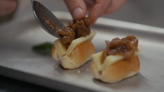 Close-up of a chef spooning caramelized onions onto mini rolls