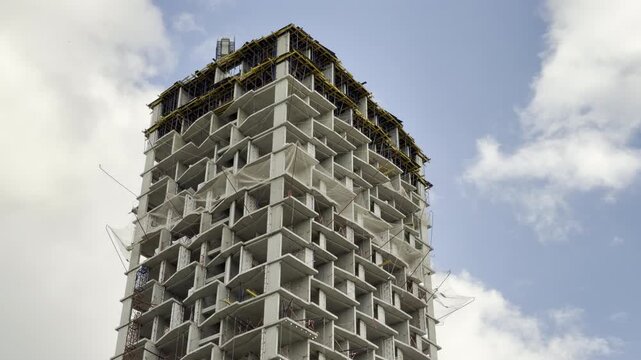 A massive concrete highrise frame stands tall during construction under shifting clouds. This incomplete structure feels powerful yet stark, inspiring a sense of quiet ambition in the landscape.