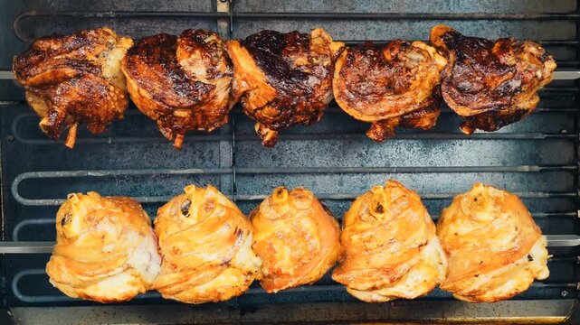 Top-down view inside an oven showing two parallel horizontal skewers: the main subject is a row of five deeply caramelized pork knuckles across