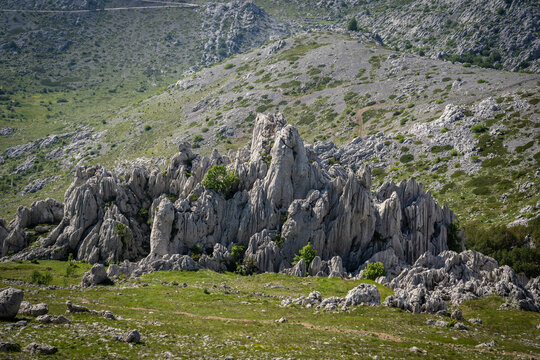 View of the jagged limestone peaks of Tulove Grede surrounded by green meadows and rocky slopes in Jasenice, Zadar County, Croatia.
