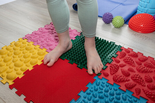 Child walking barefoot across orthopedic massage mats with different tactile textures. Concept of sensory integration, balance development, coordination, motor skills, foot health.