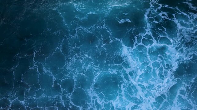 Aerial view of crashing waves in slow motion with a fixed top view showing water movement at the beach during the daytime