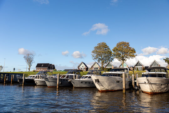Modern luxury boats moored at Zwartsluis Netherlands canal marina bright sunlight modern houses trees background. Calm water reflects the vessels and blue sky, creating a serene Dutch coastal scene
