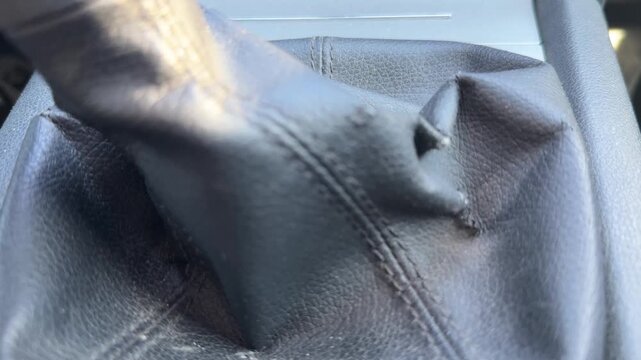 Driver changes gears using a manual transmission lever in a car, close-up of worn leather shift boot, everyday driving, vehicle operation, automotive mechanics.