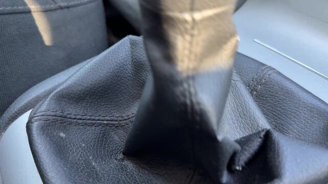 Manual transmission gear lever moves between positions inside a car, close-up of black leather shift boot, gear selection, driving technique, vehicle control.