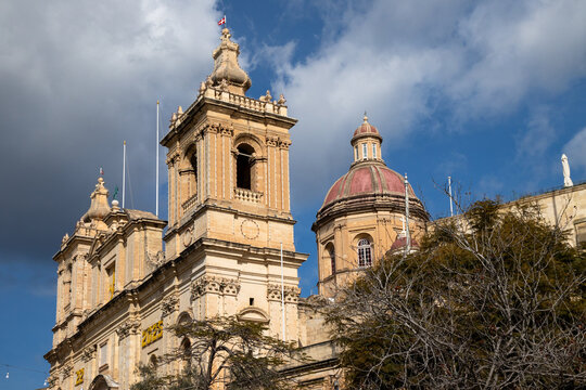 Parish Church of St Lawrence with ornate bell towers and red dome against dramatic sky in Malta