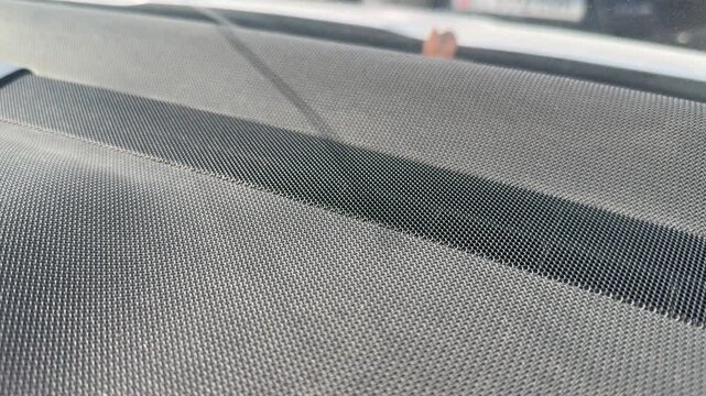 Close-up of perforated speaker grille fabric across a car dashboard, textured vehicle interior surface, automotive audio system, interior detail.
