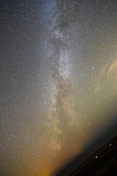 View of the Milky Way galaxy stretching across the starry night sky over the dark coastal horizon of El Cotillo, Canary Islands, Spain.