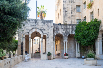 Fototapeta premium Jerusalem, Israel, June 13, 2026. An outdoor stone courtyard with arched arcades where a photographer stands taking a picture of the historic architecture. International YMCA