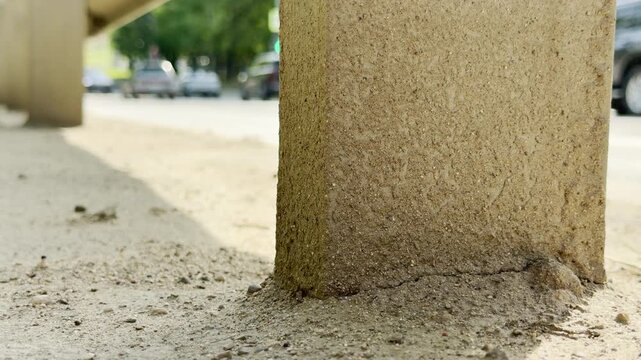 Cars travel down a bright metropolitan road next to a solid concrete post. Their steady acceleration creates a loud, continuous roar of traffic.