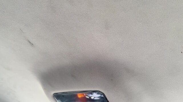 Close-up of the fabric headliner and dome light in a car ceiling, vehicle interior detail, cabin lighting, automotive upholstery, passenger compartment.