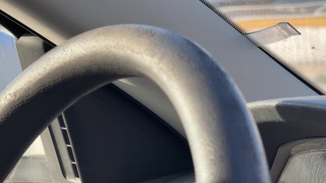Close-up of a black steering wheel and dashboard inside a car, driver perspective, vehicle control, automotive interior, everyday road travel.