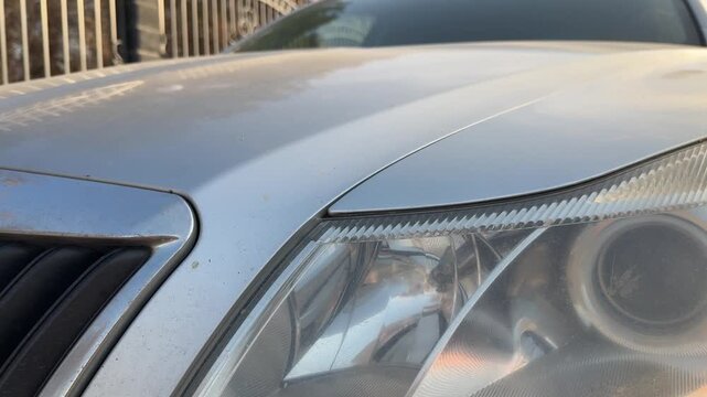 Front turn signal flashes beside the headlight and grille on a silver car, blinking indicator, vehicle signaling, automotive lighting, road safety.