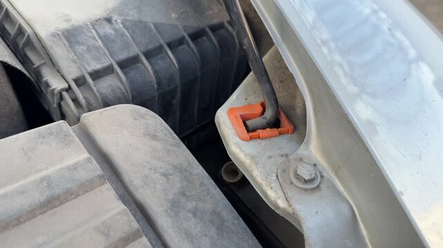 Hood support rod is released from its retaining clip inside a car engine bay, vehicle maintenance, engine access, automotive repair, mechanical inspection.