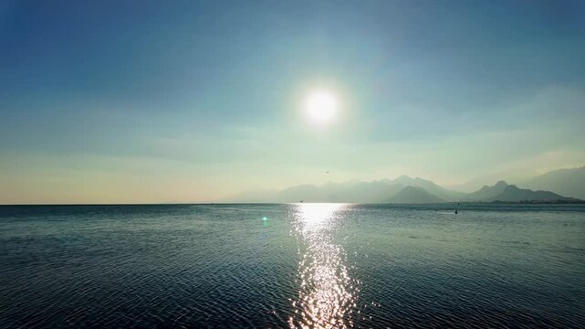 Sun shines over calm mediterranean sea with misty taurus mountains and antalya cliff coastline.