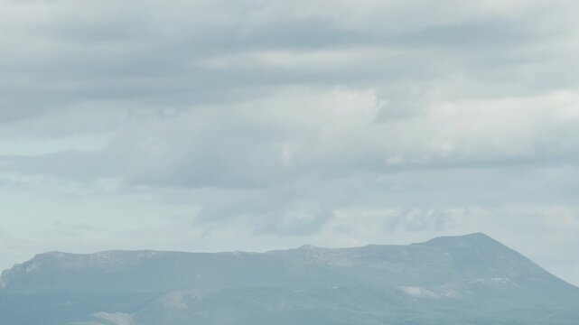 Dense grey clouds cover most of the sky. The heavy layers of cloud hang low over a distant, hazy mountain range on an overcast day.