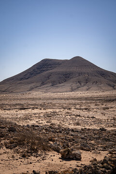 View of the Calderon Hondo volcano rising above an arid desert landscape with volcanic rocks under a clear blue sky in Las Palmas, Canarias, Spain.