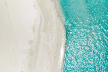 Obraz premium Aerial view of Maldives shoreline shows powder white sand meeting clear turquoise water. Gentle waves shimmer in bright daylight, with sandbars visible and no people present.