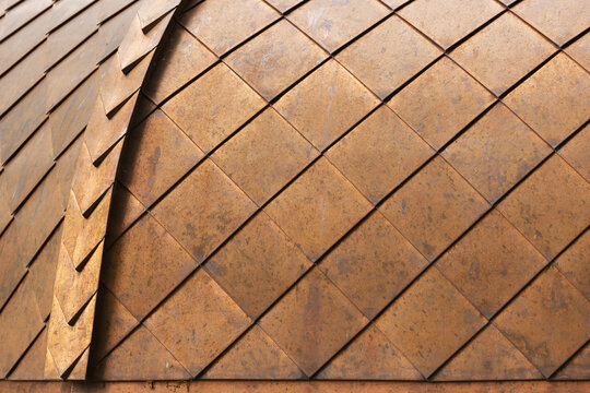 Close-up of copper metal tiles forming a repeating geometric pattern on a domed roof surface, showing rust patina, overlapping shingles and textured detail ideal for classic architecture 