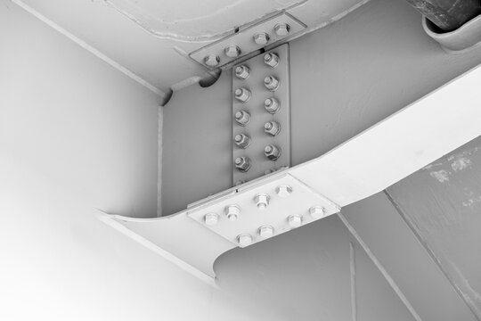 Close-up view of a painted steel beam connection showing bolts, plates and welds in an industrial structural joint beneath a bridge, emphasizing engineering, strength and architectural detail
