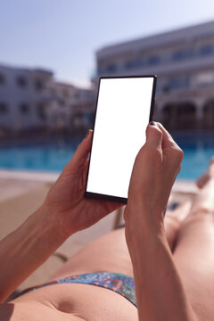 Woman relaxing by swimming pool while using smartphone with blank white screen mockup.