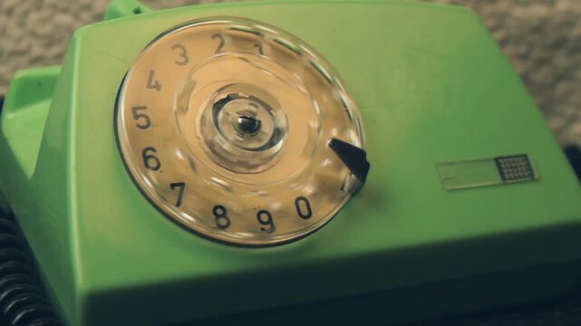 Extreme close-up finger turning plastic dial of retro green landline telephone. Hand dials a city number, analog communication technology from the last century