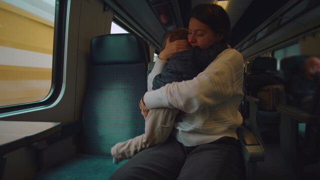Mother embraces toddler after minor bump on train kissing head to comfort pain conveying protection affection healing care and emotional safety during everyday family commute