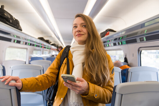Woman on Train Holding Phone and Standing in Aisle