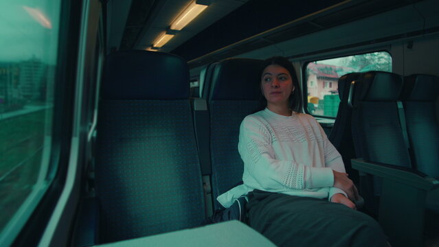 Woman sitting quietly in train carriage watching city pass by window suggesting contemplation independence everyday travel experience emotional pause and modern life movement