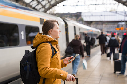 Woman at Train Station With Suitcase and Phone in Hand