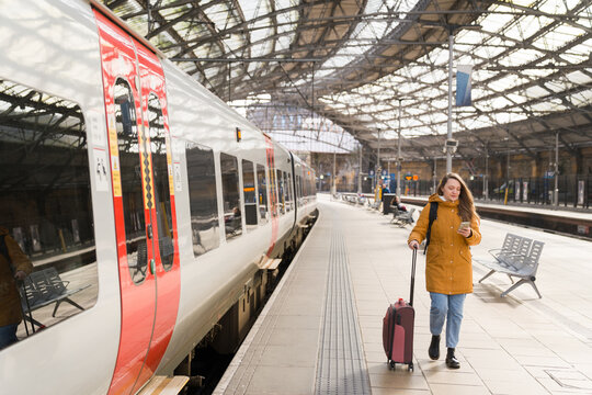 Woman Walks With Suitcase and Phone in Train Station