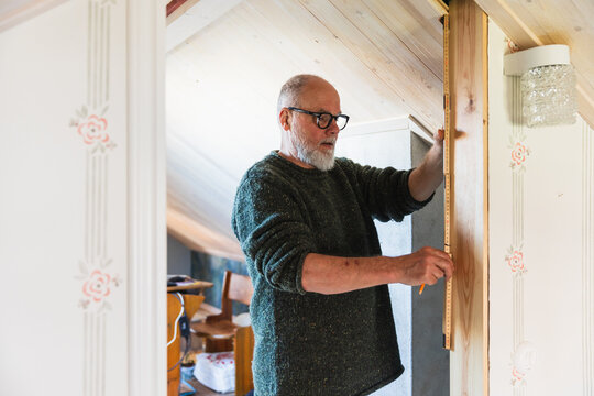 Mature Man Using Folding Ruler in Wooden Attic
