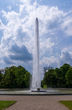 A tall impressive fountain spraying water high into the sky over a pool in the Herrenhausen Gardens in Hannover, Lower Saxony, Germany. Bright sky.