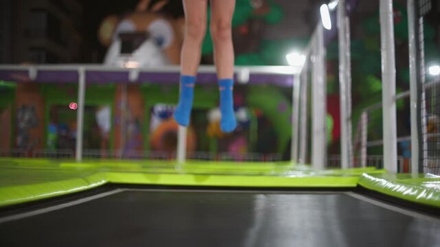 Young blonde girl bouncing on trampoline at indoor amusement park, wearing grip socks, colorful play area with mascots in background, active fun leisure
