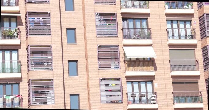 Close view of a modern residential apartment building facade featuring balconies, windows, shutters and brick exterior. Urban housing architecture detail on a sunny day in Madrid, Spain.