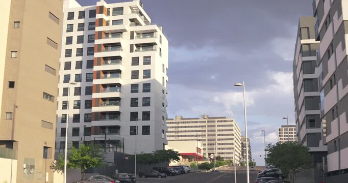 Street view of modern residential apartment buildings in an urban neighborhood with parked cars, trees and contemporary housing architecture. City living and residential development in Madrid, Spain.