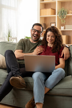 Multiracial young couple watching computer laptop sitting on the sofa at home - Happy diverse husband and wife using pc online services - Technology life style concept