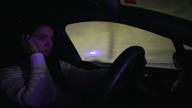 Woman driving at night resting hand near face while steering conveying tiredness contemplation steady attention and disciplined control during late evening commute