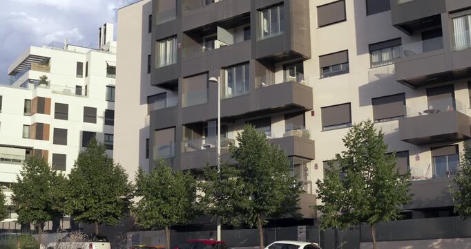 Street view of modern residential apartment buildings with glass balconies, contemporary facades and urban trees. Residential housing architecture in a modern neighborhood of Madrid, Spain.
